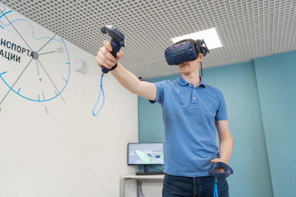 Person wearing a virtual reality headset and holding two VR controllers, standing in a modern room with light blue walls and a white patterned ceiling.